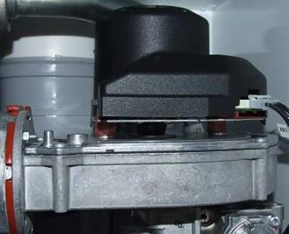 Remeha Gebläse mit schwarzem Gehäuse und metallischer Grundstruktur. Anschlussleitungen sichtbar, montiert auf einer Heizungsanlage.